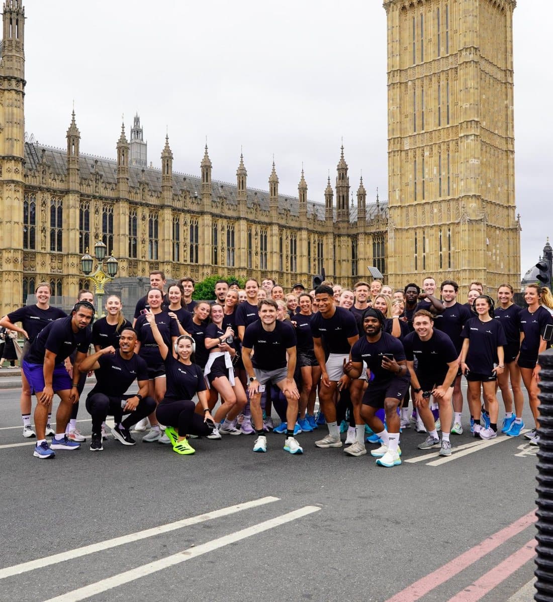 A big group of runners in PacePal t-shirts posing together on Westminster Bridge, with the Houses of Parliament and Big Ben behind them